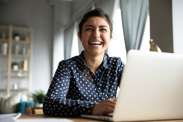 Cheerful indian girl laughing sit with laptop at table