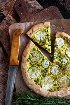 Homemade courgette and goat cheese pie on a dark rustic wooden board background