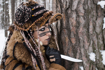 Portrait of a hunter's girl in fur clothes, which holds a knife stuck in the bark of a pine