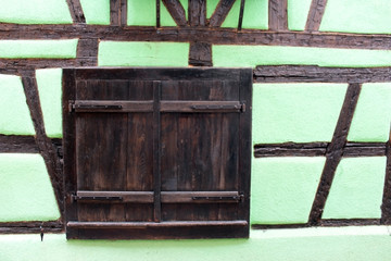 Old closed shutter window with brown doors on a light green typical french house wall