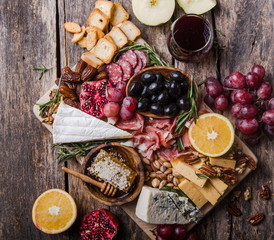 Traditional italian antipasto plate. Assorted cheeses on wooden cutting board. Brie cheese, cheddar slices, gogonzola, walnuts grapes, olives, prosciutto, rosemary and glass of red wine. top view
