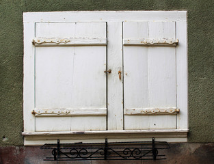 Old shutter window with closed white doors and an empty metal planter