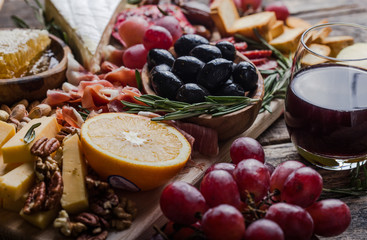 Traditional italian antipasto plate. Assorted cheeses on wooden cutting board. Brie cheese, cheddar slices, gogonzola, walnuts grapes, olives, prosciutto, rosemary and glass of red wine. top view