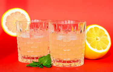 two glasses with an alcohol cocktail (lemonade, tonic) and lemon on a red background