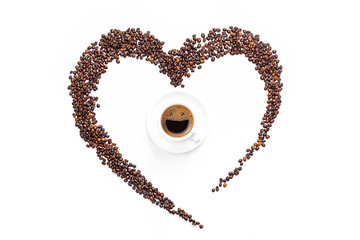 heart made from coffee beans and ground coffee on a white background. in the center is a cup of coffee, in a cup of coffee from coffee foam a happy smiling face. invigorating drink concept