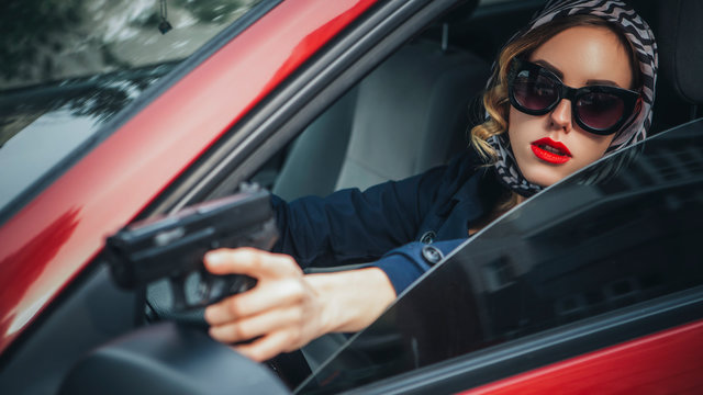 Beautiful brunette sexy spy agent (killer or police) woman in leather jacket and jeans with a gun in her hand driving a car after someone, to catch him