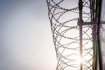 barbed wire against blue sky with sun