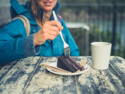 Young woman wearing raincoat eating cake outdoors