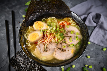 Homemade traditiona Japanese Ramen noudle soup with meat slices, egg and spring onions in dark bowl