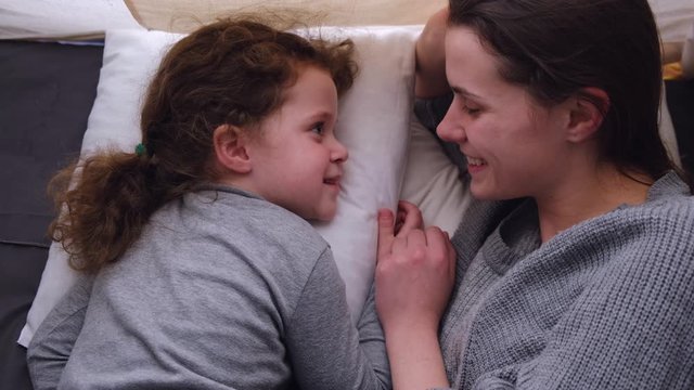 Top view on affectionate happy family single mom and cute little child daughter laughing embracing and kiss, young mother foster parent hug small kid girl cuddling touching in children's room in tent