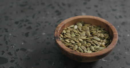 pumpkin seeds in olive bowl on terrazzo countertop with copy space