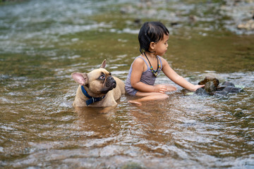 cute asian girl playing with her lovely french bulldog at stream in nature.