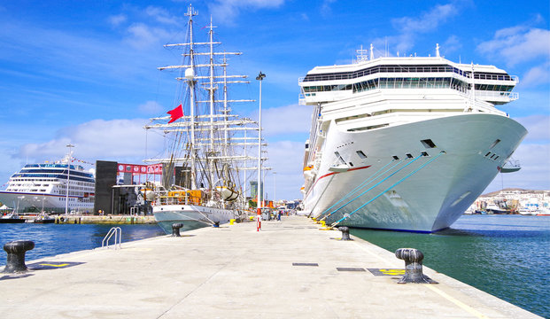 Gigantic white modern Carnival Cruise Lines cruise ship liner with other ships and windjammer in port of Gran Canaria on sunny day with blue sky during Transatlantic cruising