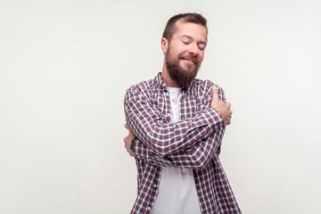 Love yourself. Portrait of smiling confident bearded man in plaid shirt embracing himself with...