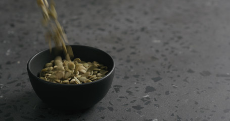 dried pumpkin seeds falling into black bowl on terrazzo countertop