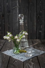 A glass of vodka with pickled cucumber on a fork against a glass decanter and a dark wooden...
