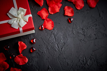 Gift box on black stone table. Romantic holiday background with rose petals