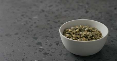 pumpkin seeds in white bowl on terrazzo countertop with copy space