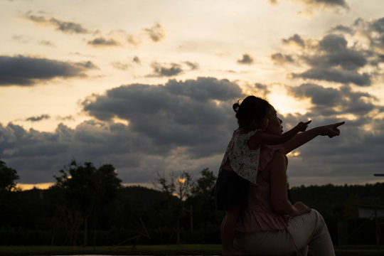 Silhouette picture of mother and daughter sitting outdoor.