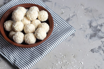 Candies in coconut flakes and fresh coconut with flax seeds on a gray stone background. Energy balls.