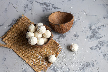 Candies in coconut flakes and fresh coconut with flax seeds on a gray stone background. Energy balls.
