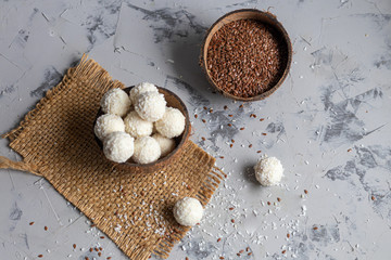 Candies in coconut flakes and fresh coconut with flax seeds on a gray stone background. Energy balls.