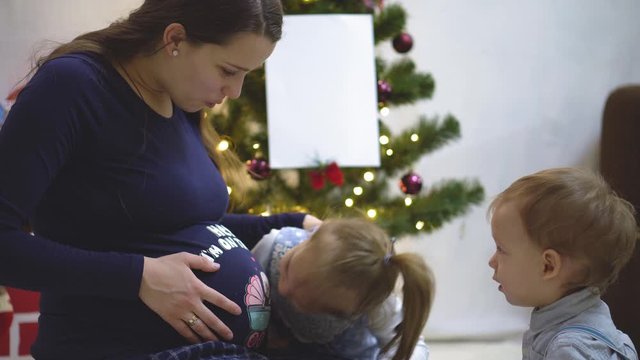 Two children grope listen and kiss the belly of a pregnant mother