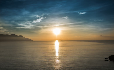 Sunrise over a calm sea against the background of the islands. The rising sun is reflected on the sea surface.