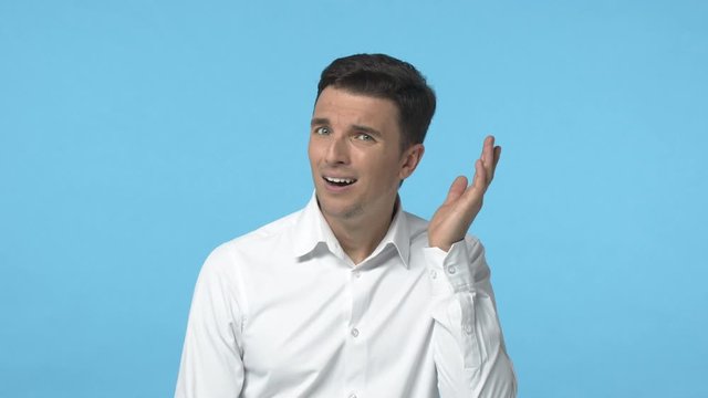 Slow-motion attractive distressed adult man in white shirt, cant hear you, touching ear and asking speak louder, dont understand what person say, standing blue background confused