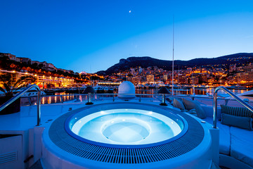 Jacuzzi on the yacht and buildings with lit lights in the distance in Monaco