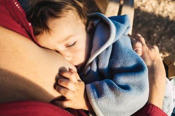 Baby naps while being breastfed by his mother outdoors.