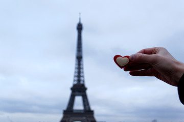 a man's hand holds a red heart against the background of the Eiffel tower, in the most romantic city