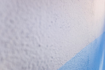 Blue and white bicolor background of a textured wall illuminated laterally by sunlight.