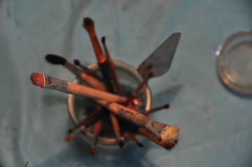 Used Paintbrushes and Palette Knife in Cup on Blue Background