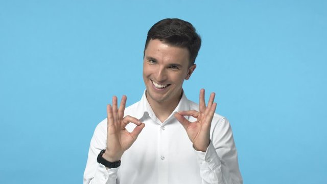 Alright, you got this. Slow motion confident, upbeat smiling caucasian male in white shirt, encourage all good, showing okay gesture and grinning, reassure everything fine, got under control