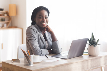 Successful businesswoman sitting at workplace in office and smiling to camera