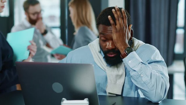 Close up view of sad tired african american handsome business man touching head working hard on laptop upset exhausted young office work worried sleepy stressed frustrated employee corporate. Portrait