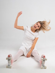 Beautiful woman shaking her head with her blonde hair flying around and sitting on a white floor in a vintage roller skates shoes