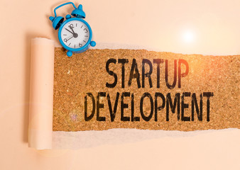 Writing note showing Startup Development. Business concept for efficiently develop and validate scalable business model Alarm clock and torn cardboard on a wooden classic table backdrop