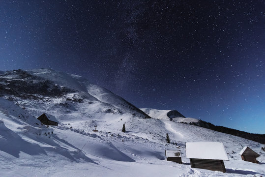 Fairytale landscapes of the winter Carpathian Mountains with a charming milky way in the sky tourist tents and snowy houses in the valleys	