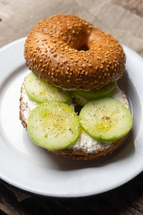 Sesame bagels with spreadable cream cheese and cucumber on wooden background