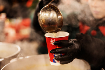 Unrecognizable street vendor pours hot mulled wine into a disposable cup. Traditional winter drink...