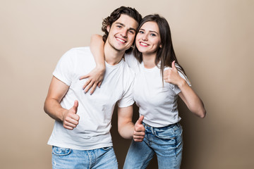Fototapeta premium Portrait of beautiful people man and woman in basic clothing posing together at camera with thumbs up isolated over beige background