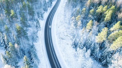 Car driving through the winter forest on country road. Top view from drone