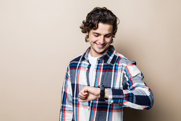 Portrait of young man looking at his watch isolated on beige background