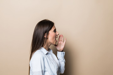 Side view of young woman in casual clothes looking aside, screaming with hands near mouth isolated on pastel beige background in studio. People sincere emotions, lifestyle concept.