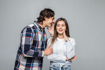 Naklejka premium Secret and people concept. Young happy couple whispering over grey background