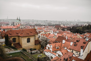 Obraz premium Panorama of Prague with red roofs and Church. City view of Praha old city. Rustic grey colors toning.
