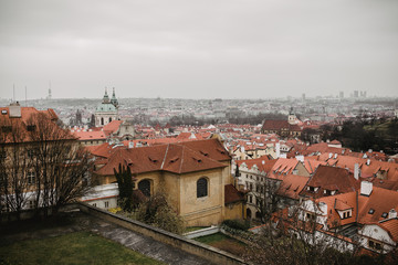 Fototapeta premium City of Prague with red roofs and Church in fog. City view of Praha old city. Rustic grey colors toning.