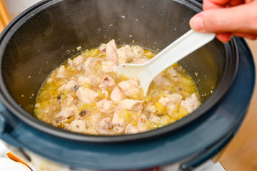 Woman stirs the stew with a white spoon in a slow cooker.